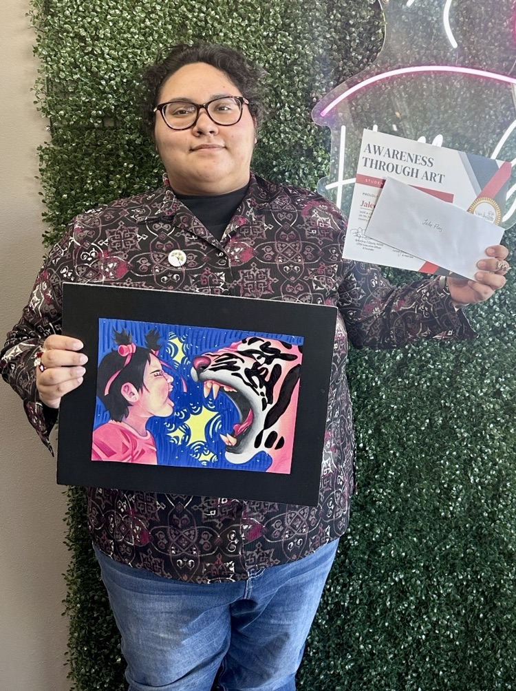 Alt text: Student Jaelee Flores holds her colorful artwork “Hear the Roar” and her first-place award at the Awareness Through Art Show.