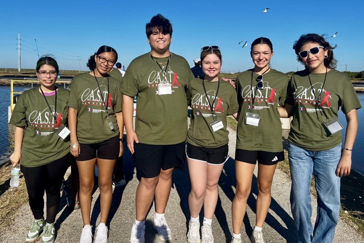 Group of students posing together near the water in matching event shirts.