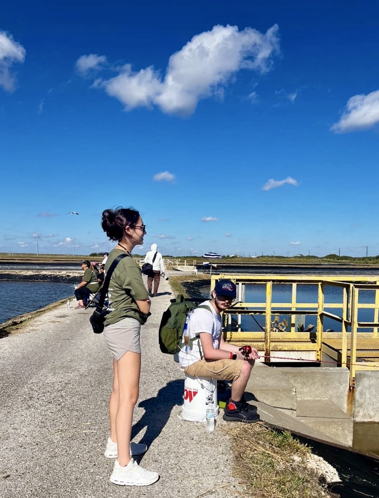 Group of students posing together near the water in matching event shirts.