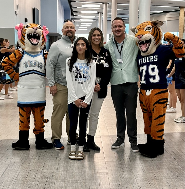Alt Text: Eliana Lucio stands with Carroll staff and supporters wearing “Carroll XC State 2025” shirts, celebrating her state qualification with smiles, school spirit, and Tiger mascots.