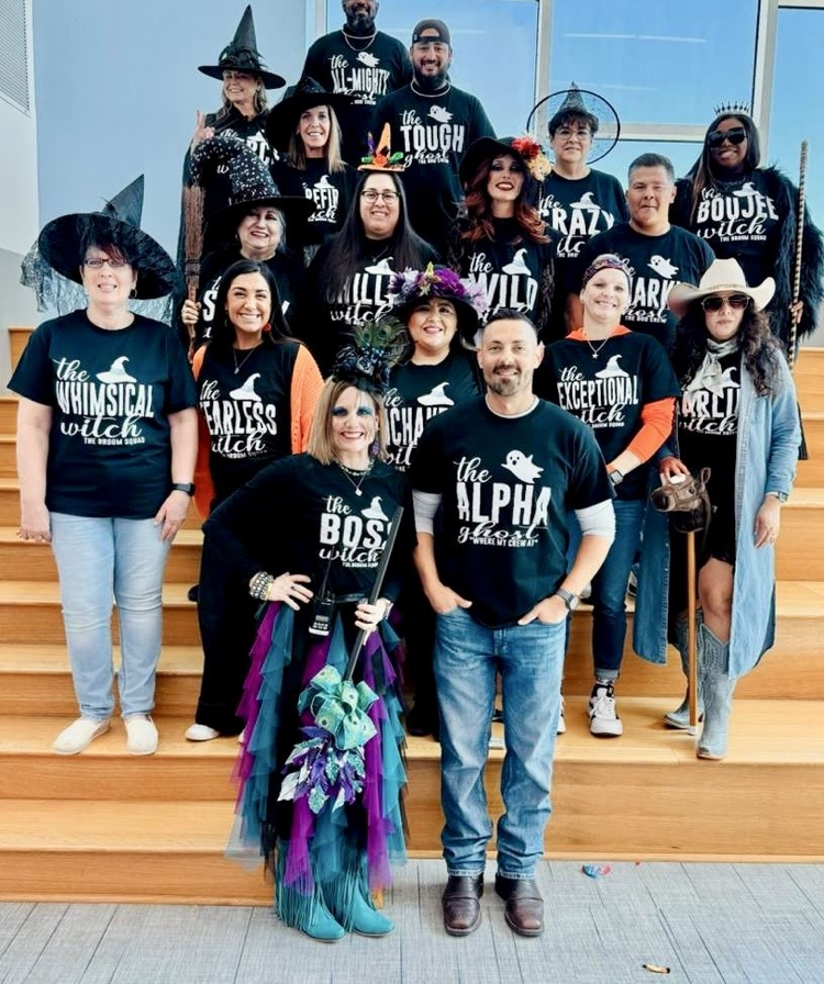 : Group photo of Carroll High School’s Special Education team dressed in themed “witch” shirts and hats, smiling together on the stairs for Halloween. 