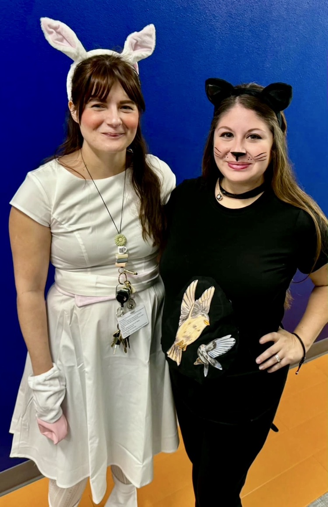 Three English teachers dressed as Animal Farm characters — one in a plaid shirt and cowboy hat, one in a white bunny outfit, and one in black cat ears and whiskers — posing together in front of a blue wall.