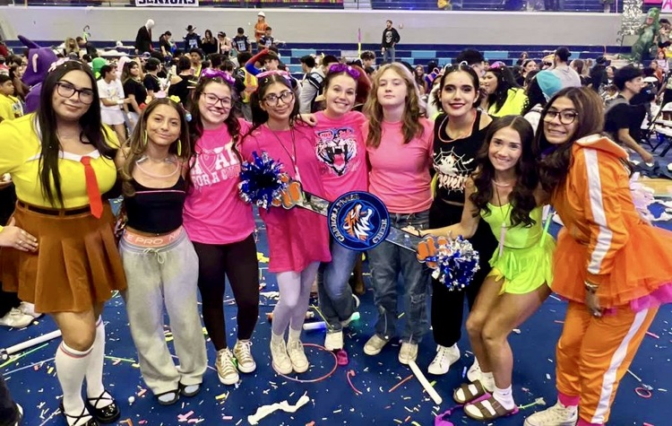Group of Carroll High School juniors dressed in colorful outfits posing in the gym after winning the Spirit Stick at the pep rally; confetti on the floor and cheering crowd in the background.