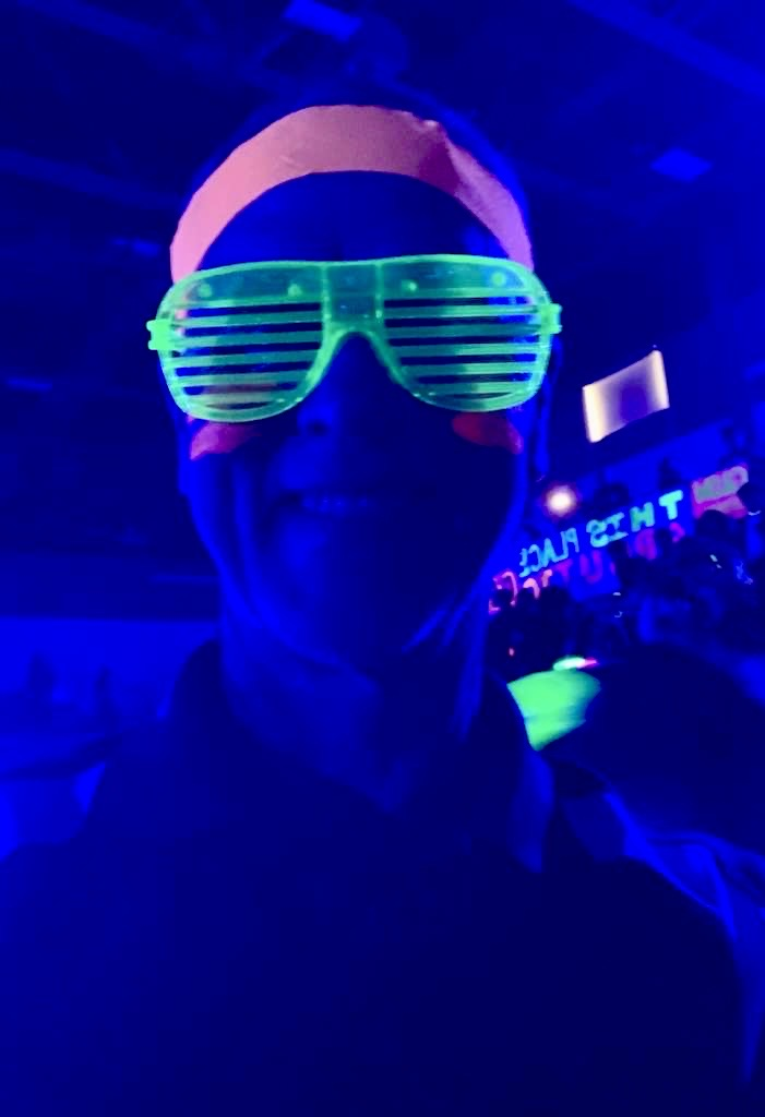  CTE teacher Mr. Rousseau wearing neon green shutter shades glowing under blacklight during Carroll High School’s blackout pep rally.
