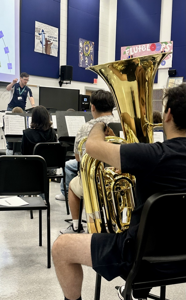 Band students practicing for a concert; percussion and tuba sections are focused while a student plays timpani drums in the foreground.