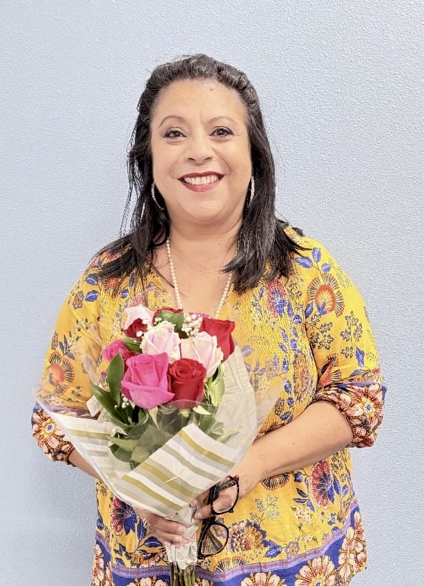 Dr. Melissa Hernandez smiling while holding her bouquet of flowers against a light blue wall.