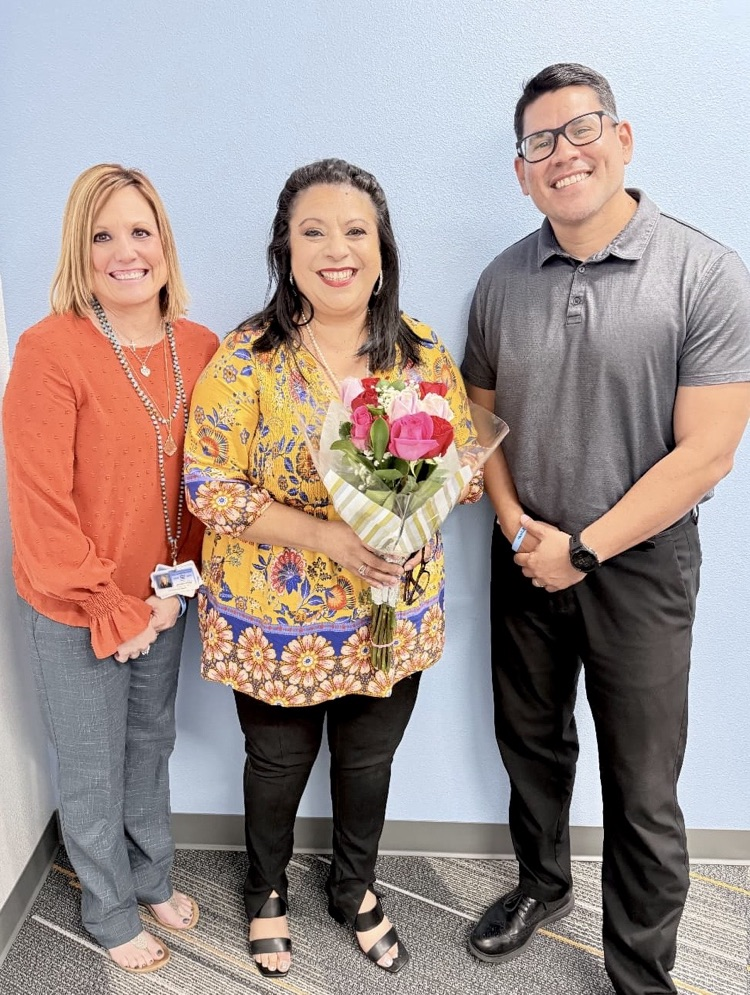 Dr. Melissa Hernandez smiling while holding her bouquet of flowers against a light blue wall.