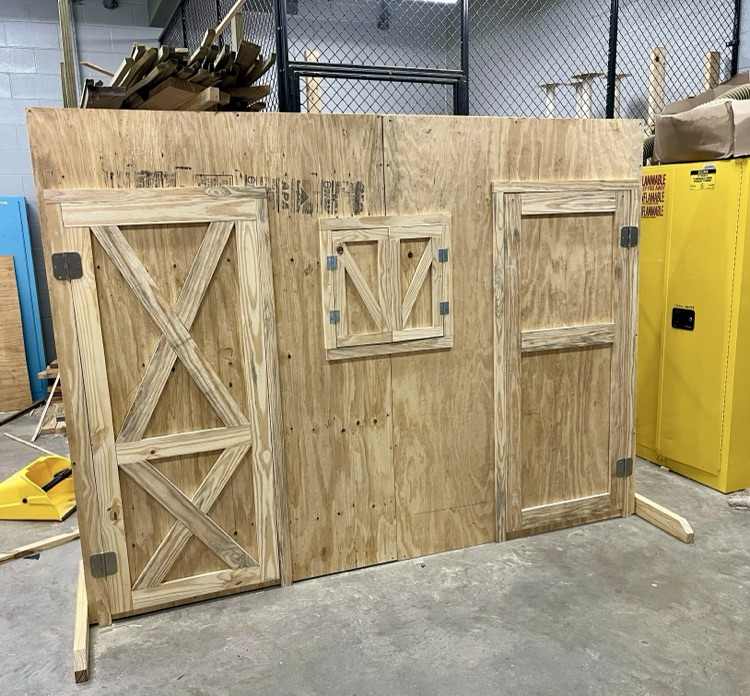 Construction students built and painted a wooden barn-style prop for FFA’s competition, showing progress from unfinished wood to the completed gray and white display.