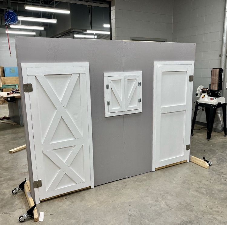 Construction students built and painted a wooden barn-style prop for FFA’s competition, showing progress from unfinished wood to the completed gray and white display.