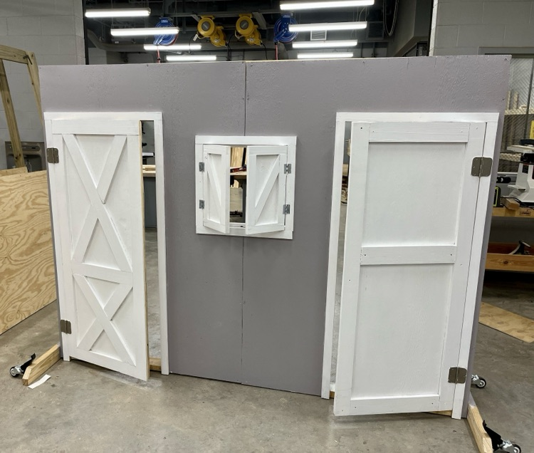 Construction students built and painted a wooden barn-style prop for FFA’s competition, showing progress from unfinished wood to the completed gray and white display.