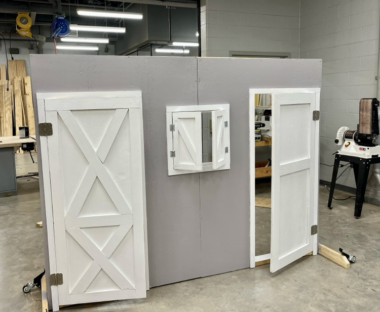 Construction students built and painted a wooden barn-style prop for FFA’s competition, showing progress from unfinished wood to the completed gray and white display.