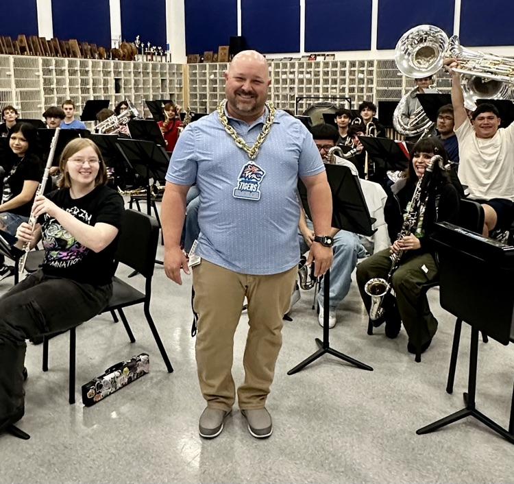 Carroll High School Band Director Kyle Sorrows, smiling and wearing a gold chain, poses with his band students in the rehearsal room, celebrating his recognition as Staff of the Week.