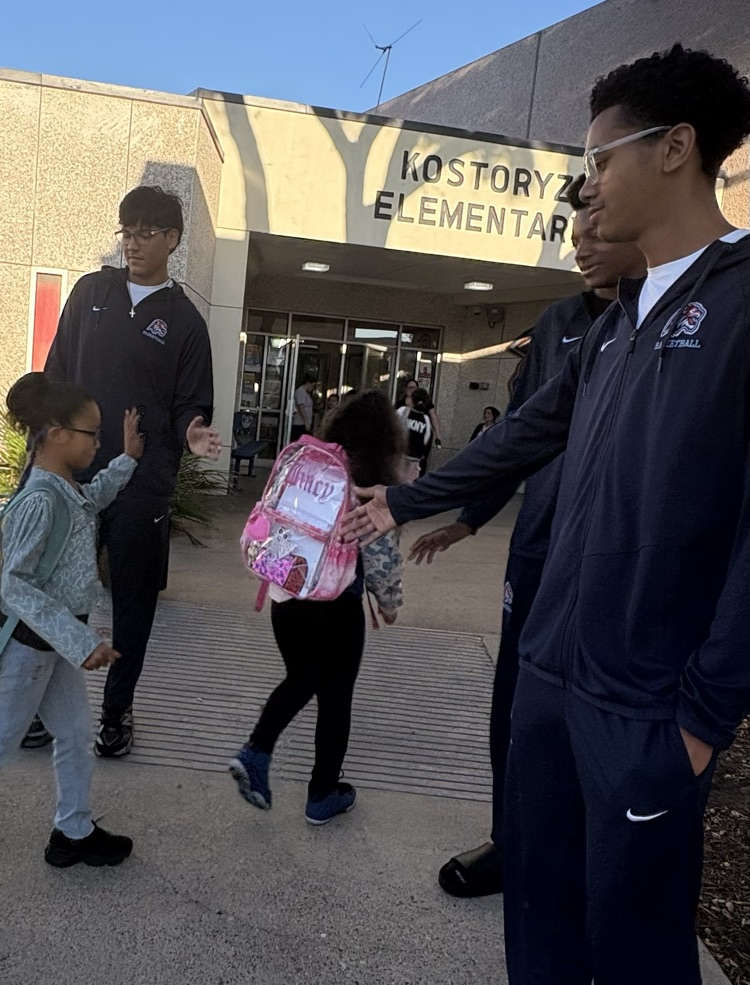 Alt Text: Carroll High School basketball players in navy warm-ups greet elementary students with smiles, fist bumps, and high-fives at Kostoryz Elementary, spreading school spirit as the basketball season begins.