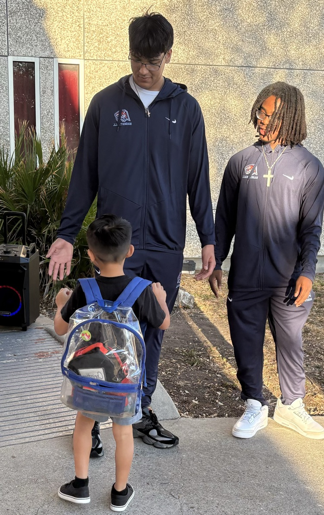 Alt Text: Carroll High School basketball players in navy warm-ups greet elementary students with smiles, fist bumps, and high-fives at Kostoryz Elementary, spreading school spirit as the basketball season begins.