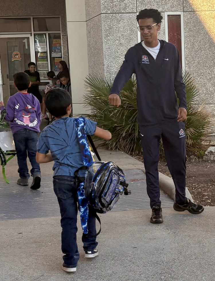Alt Text: Carroll High School basketball players in navy warm-ups greet elementary students with smiles, fist bumps, and high-fives at Kostoryz Elementary, spreading school spirit as the basketball season begins.