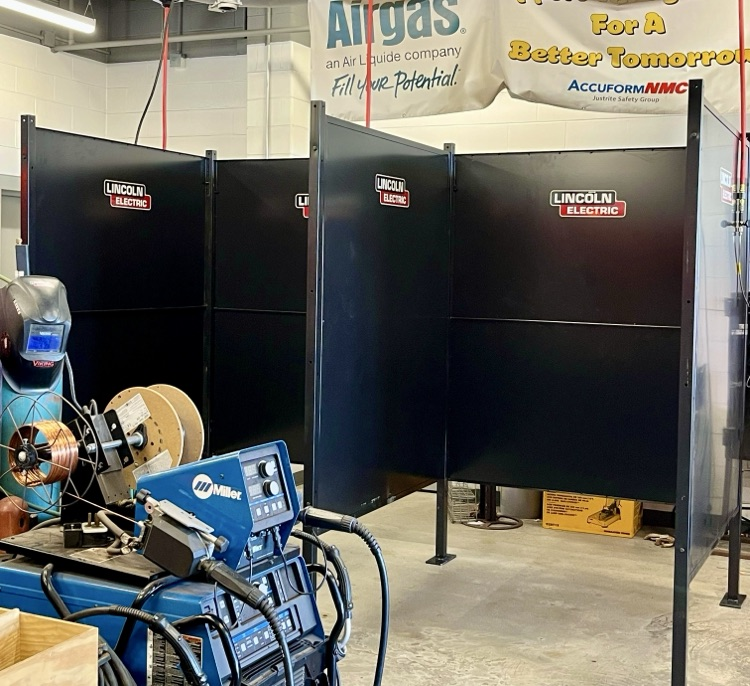 Two new black Lincoln Electric welding booths set up inside a high school welding shop.