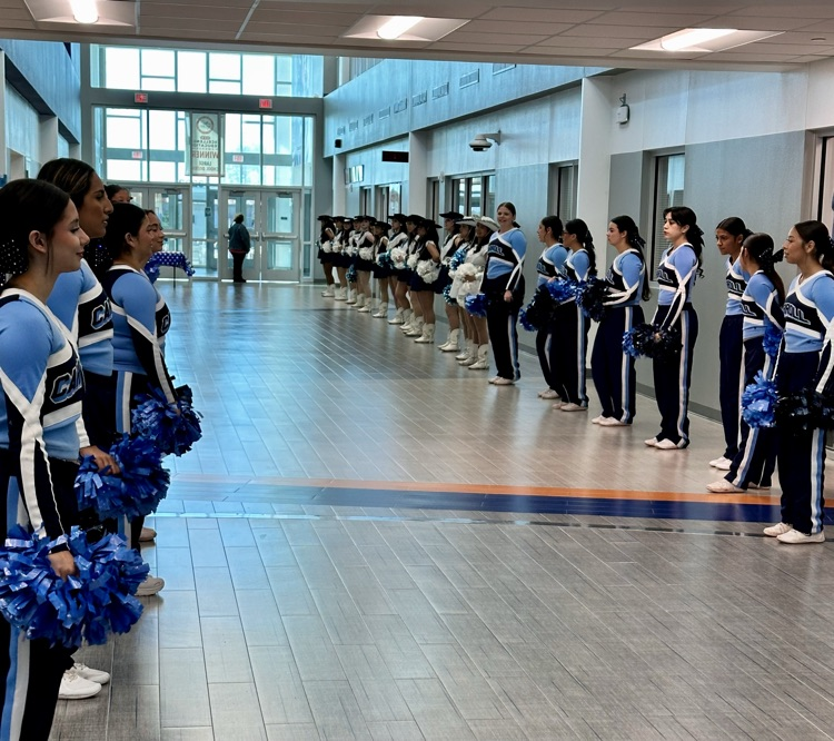 Alt text: Carroll High School students smile and wave small American flags during the Veterans Day 