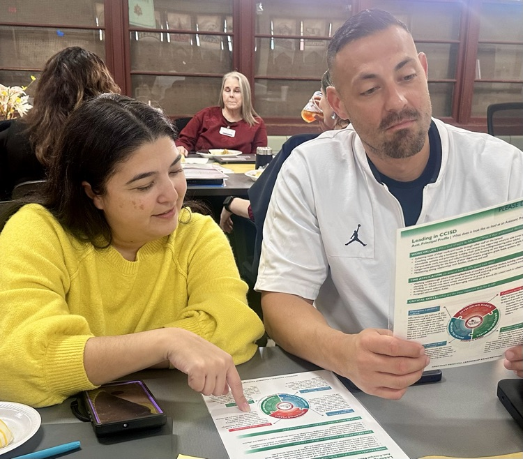 Two assistant principals collaborate during a district leadership training, reviewing CCISD’s Leadership Definition handout together at a table.