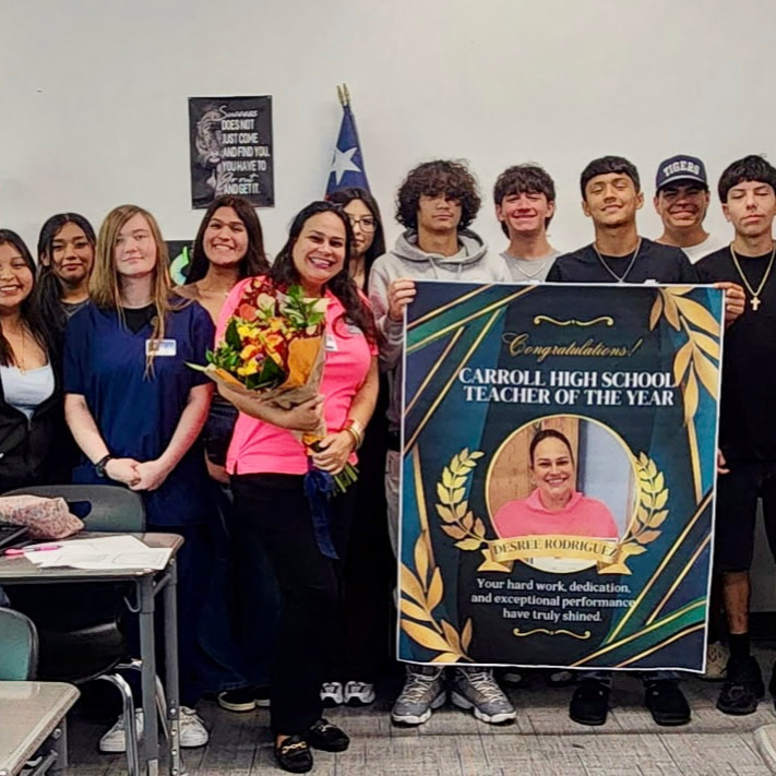 “Teacher holding flowers and posing with a Teacher of the Year banner alongside students and staff.” 
