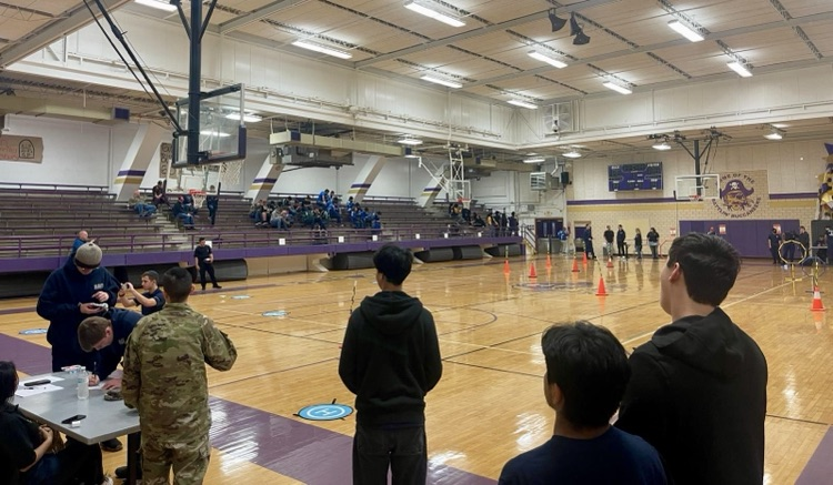 ⸻ Alt Text: Image 1: Four NJROTC cadets stand together indoors wearing Carroll and Navy hoodies. They’re smiling and holding a tall purple-and-gold trophy with a “1st place” plaque.