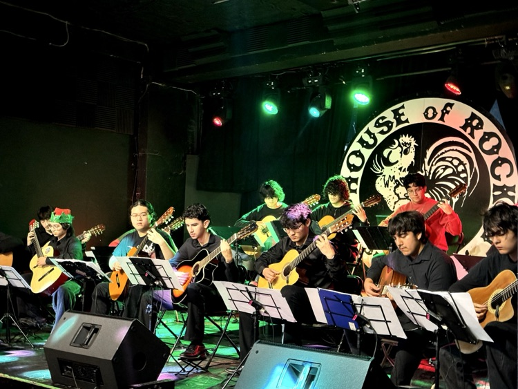 A stage full of CCISD high school guitar students performing under red and green spotlights at House of Rock.