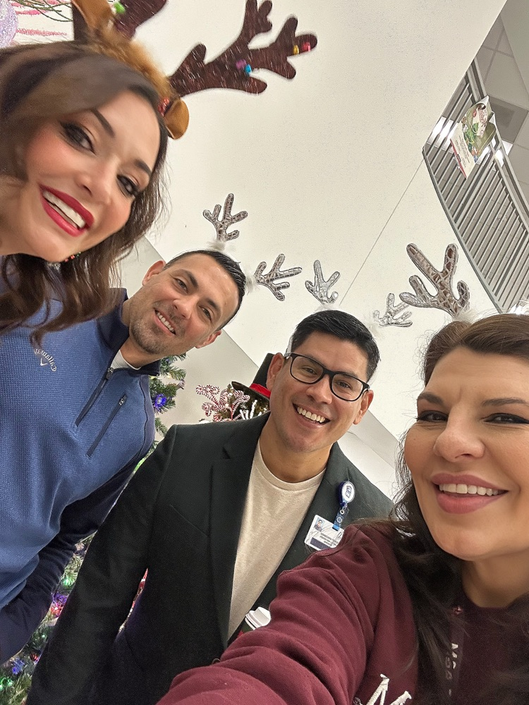 Alt Text: Four staff members smiling in a selfie while wearing festive reindeer antler headbands.