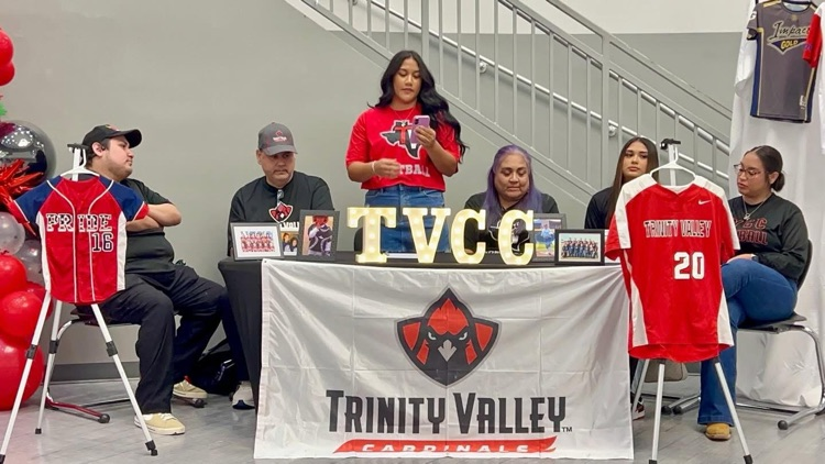 Alt Text: Talina Valdez sits at a signing table with her family during