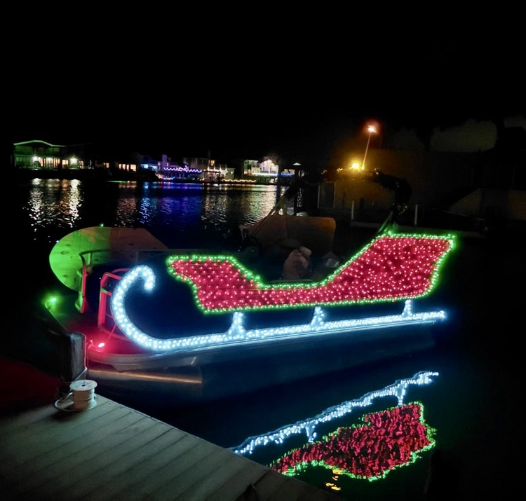 Alt Text: Students and adults stand together on a dock at night holding donated toys during a holiday toy drive,