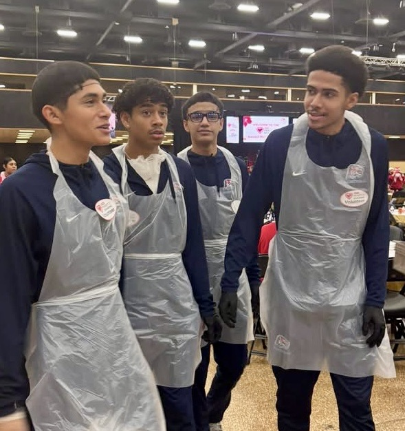 Carroll High School student-athletes wearing volunteer aprons serve meals and help at a community dinner event.