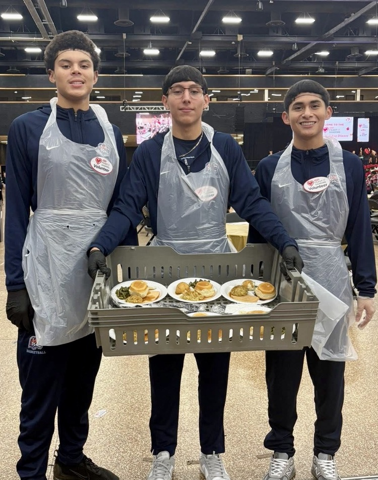 Carroll High School student-athletes wearing volunteer aprons serve meals and help at a community dinner event.