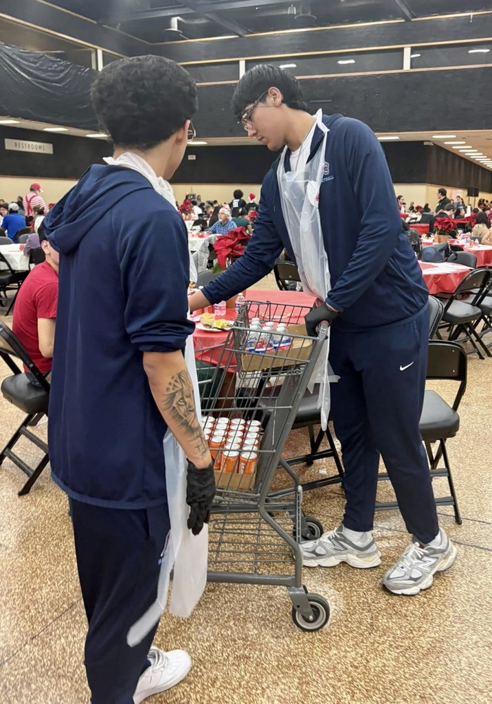 Carroll High School student-athletes wearing volunteer aprons serve meals and help at a community dinner event.