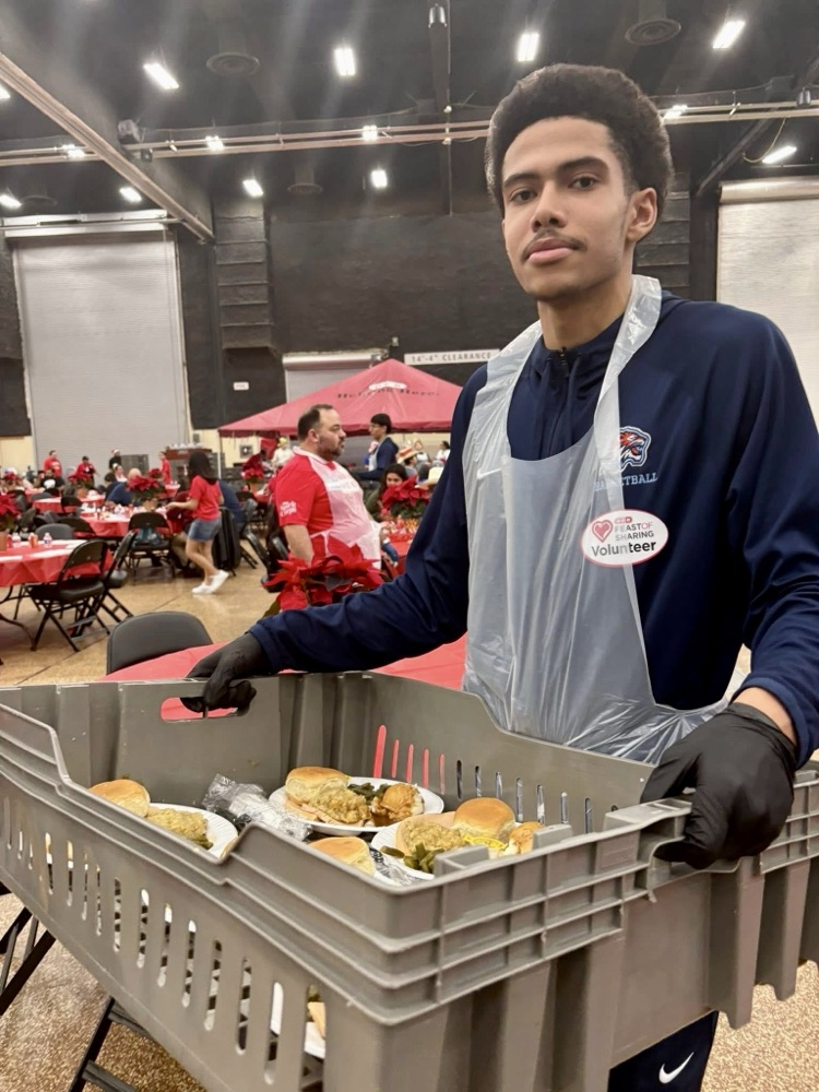 Carroll High School student-athletes wearing volunteer aprons serve meals and help at a community dinner event.