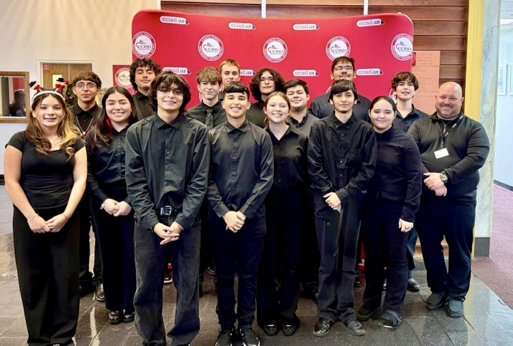 Carroll High School band students perform holiday music inside the district Administration Building, dressed in black concert attire and led by conductor Mr. Sorrows, as staff watch and listen.