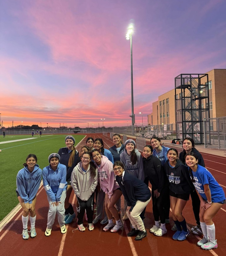 Carroll High School girls soccer team poses together on the field in blue uniforms, smiling and ready for the season, with coaches standing behind them.