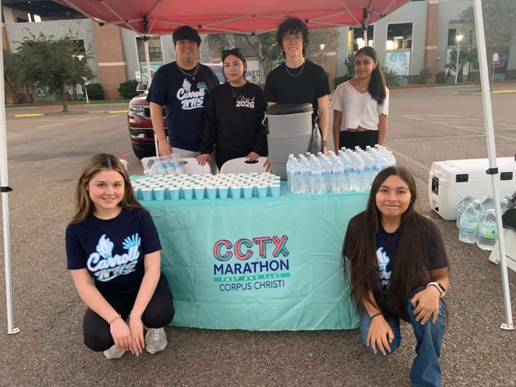 Students volunteering at a hydration station with water cups and bottles under a tent at the CCTX Marathon in Corpus Christi.