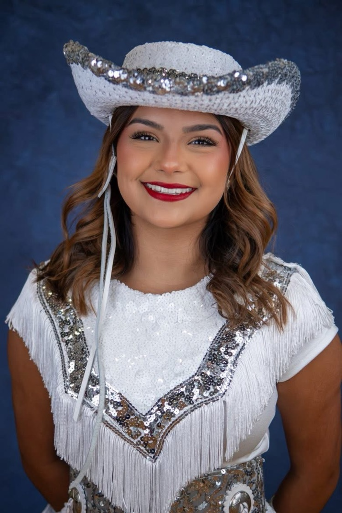 Portrait of Carroll Tigerette Isabella Cardona wearing a white and silver sequined drill team uniform and cowboy hat, smiling against a blue backdrop.