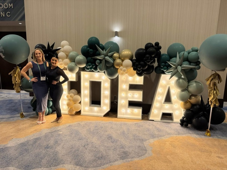 Portrait of Carroll Tigerette Isabella Cardona wearing a white and silver sequined drill team uniform and cowboy hat, smiling against a blue backdrop.