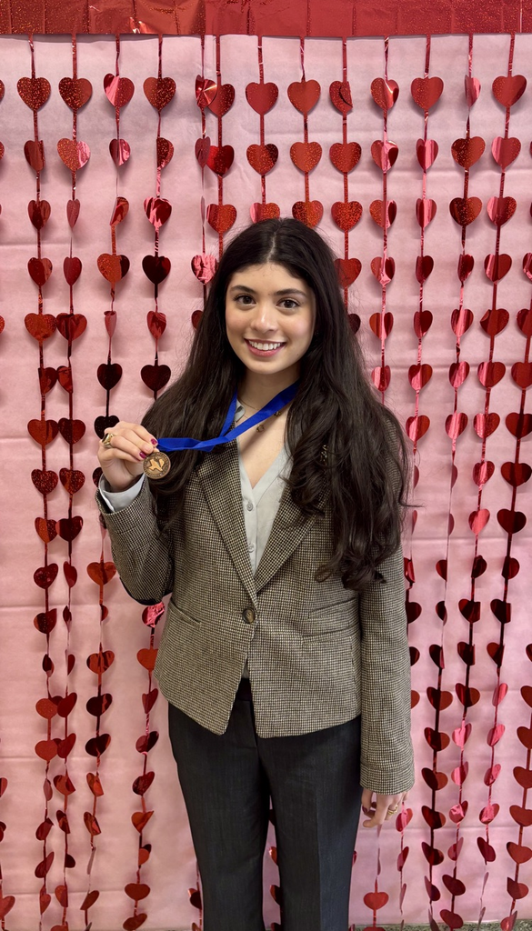 Two Carroll students smiling and holding medals in front of a red heart backdrop after placing in Academic Decathlon events.