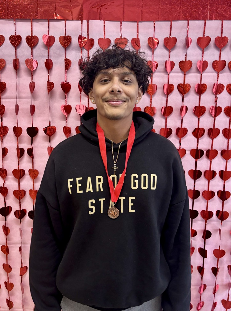 Two Carroll students smiling and holding medals in front of a red heart backdrop after placing in Academic Decathlon events.