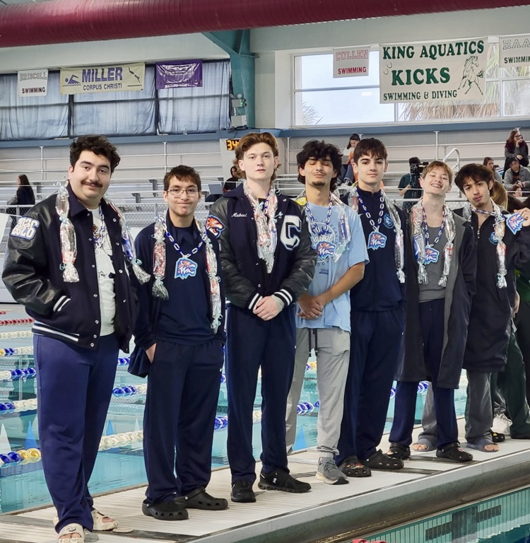 Group of Carroll High School swim seniors standing together on the pool deck wearing team apparel and senior candy leis, smiling and posing for a photo at a swim meet.