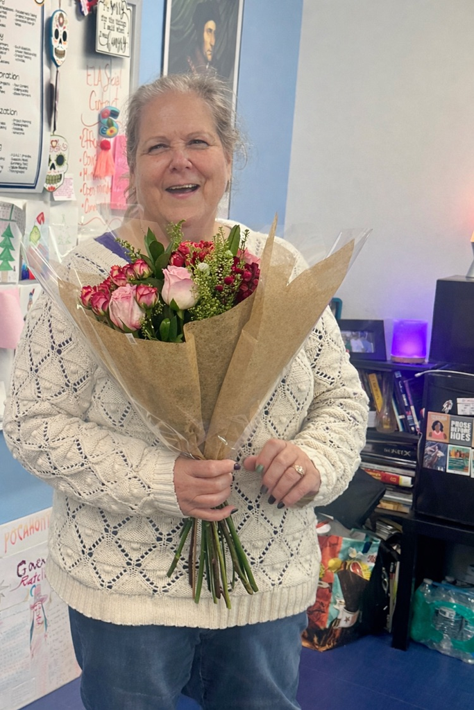 Alt Text: Ms. Sue Marshall stands in her classroom holding a bouquet of flowers and smiling. Another image shows her hugging a colleague while holding the bouquet, with student work and posters visible around the room.