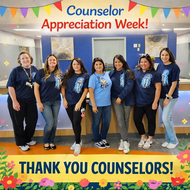Eight school counselors standing together inside a school counseling office, smiling and wearing blue Carroll shirts