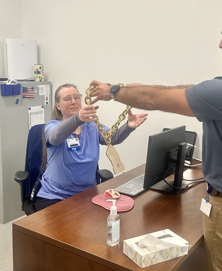 nurse in blue scrubs is smiling and holding a heart-shaped Whitman’s Sampler chocolate box, while another staff member stands beside her 