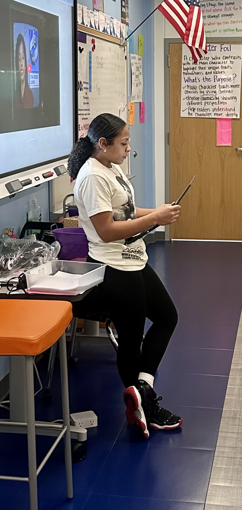 Alt Text: Students seated at desks in an English classroom, focused on reading passages, highlighting text, and writing responses on printed assignments while laptops and notebooks are open on the tables.