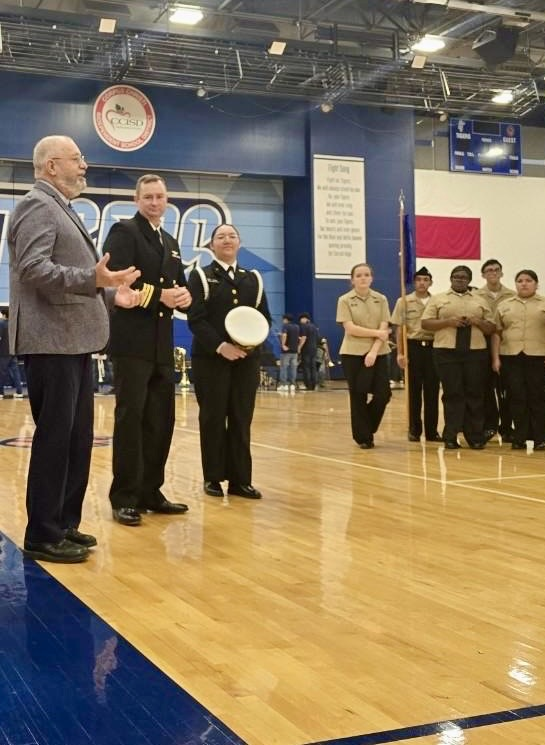 Alt text: NJROTC cadets in formal uniforms standing in formation inside a school gym during the Area Managers Inspection, including close-up and wide shots showing cadets at attention and leadership addressing the group.