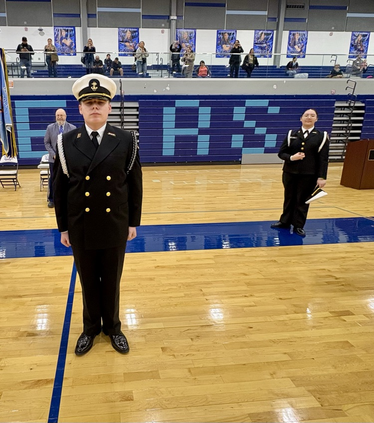 Alt text: NJROTC cadets in formal uniforms standing in formation inside a school gym during the Area Managers Inspection, including close-up and wide shots showing cadets at attention and leadership addressing the group.