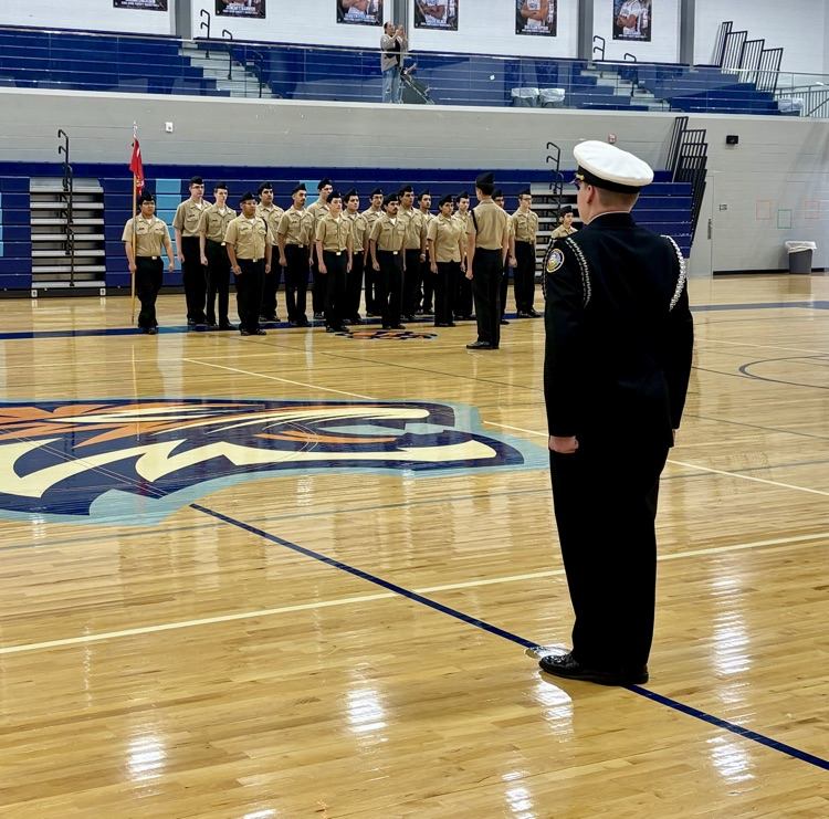 Alt text: NJROTC cadets in formal uniforms standing in formation inside a school gym during the Area Managers Inspection, including close-up and wide shots showing cadets at attention and leadership addressing the group.