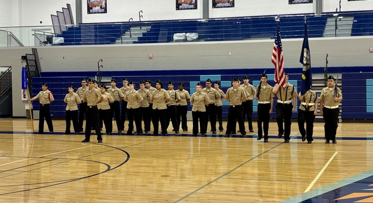 Alt text: NJROTC cadets in formal uniforms standing in formation inside a school gym during the Area Managers Inspection, including close-up and wide shots showing cadets at attention and leadership addressing the group.
