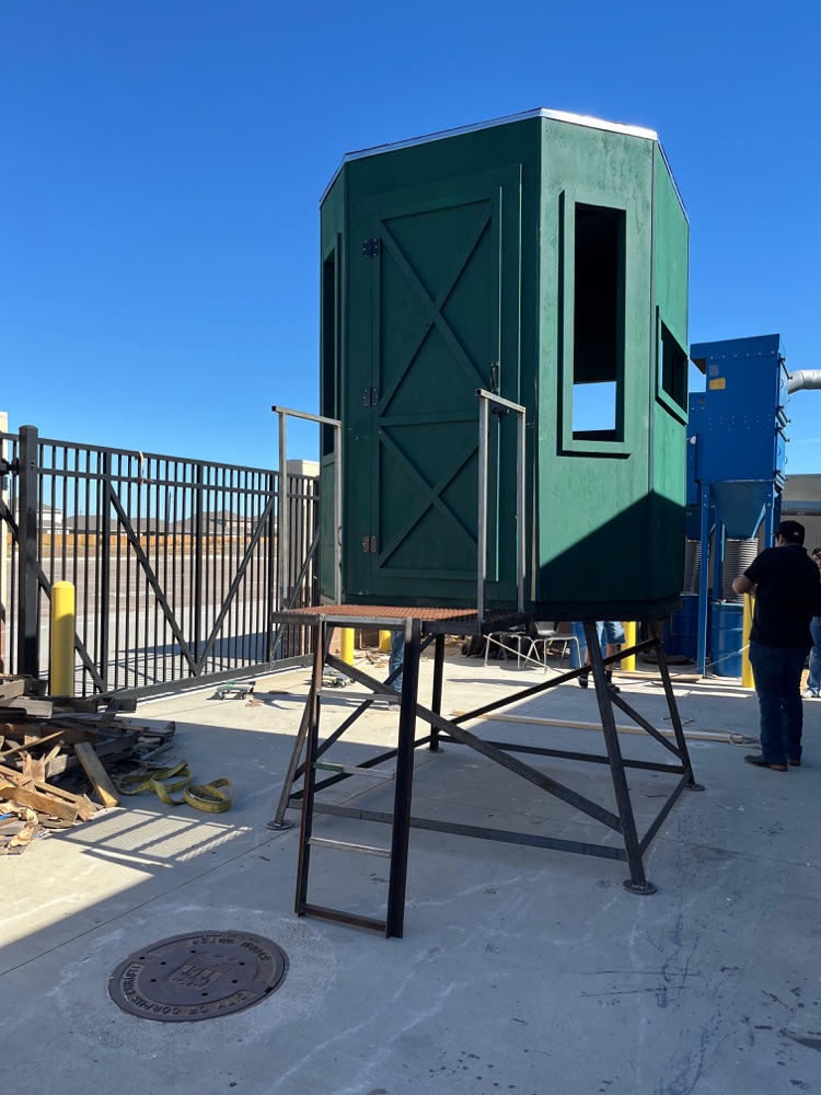 Alt text: A newly constructed metal stand supporting a green deer blind, built by student welders on campus, shown from multiple angles outdoors with clear blue skies and welding equipment nearby.