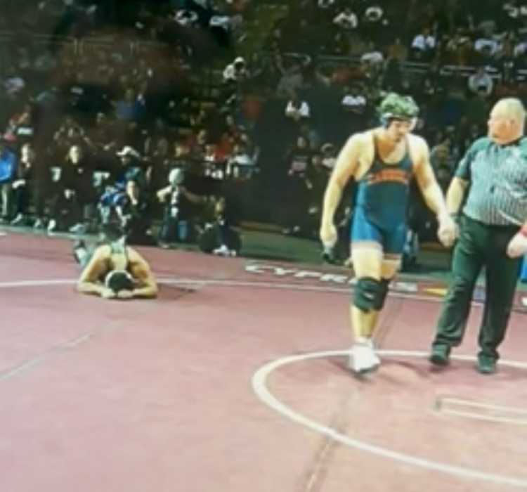 Carroll wrestler executes a takedown during a state championship match as the crowd watches in the background.